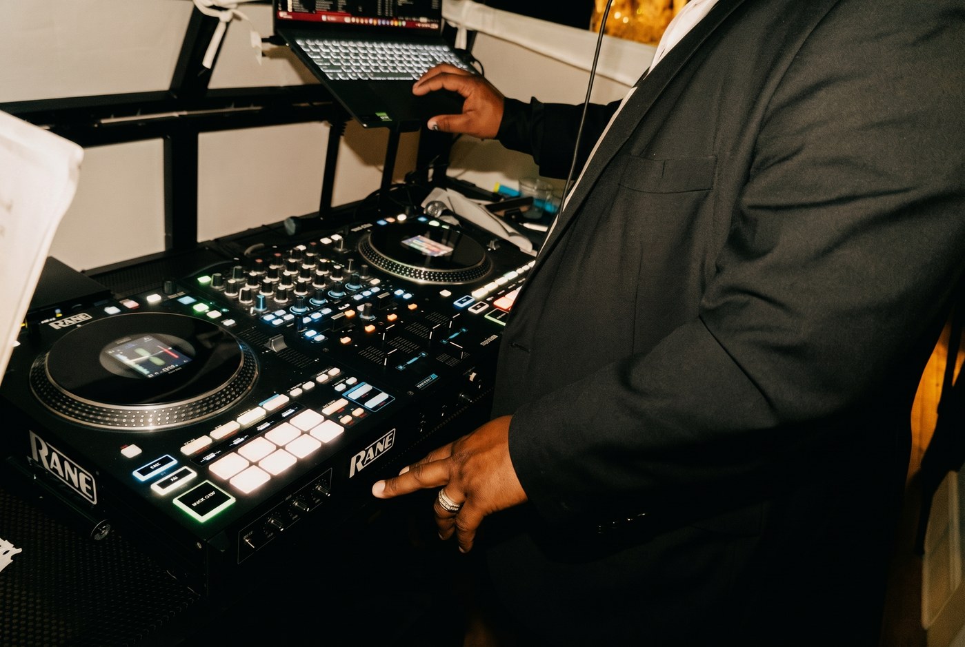 BB Events DJ in a tailored suit working a RANE controller in warm reception light.